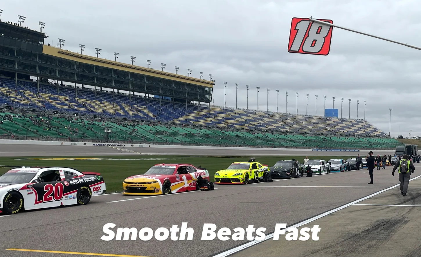 NASCAR cars lined up on pit road beneath an overcast sky
